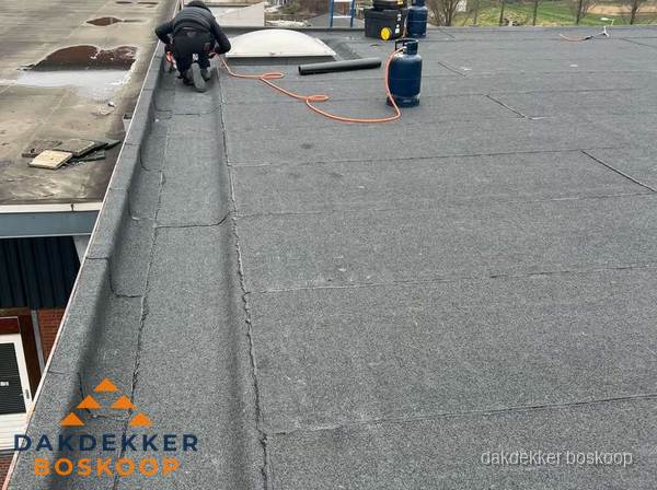 Dakdekker repareert bitumen dakbedekking op groot plat dak in Boskoop
